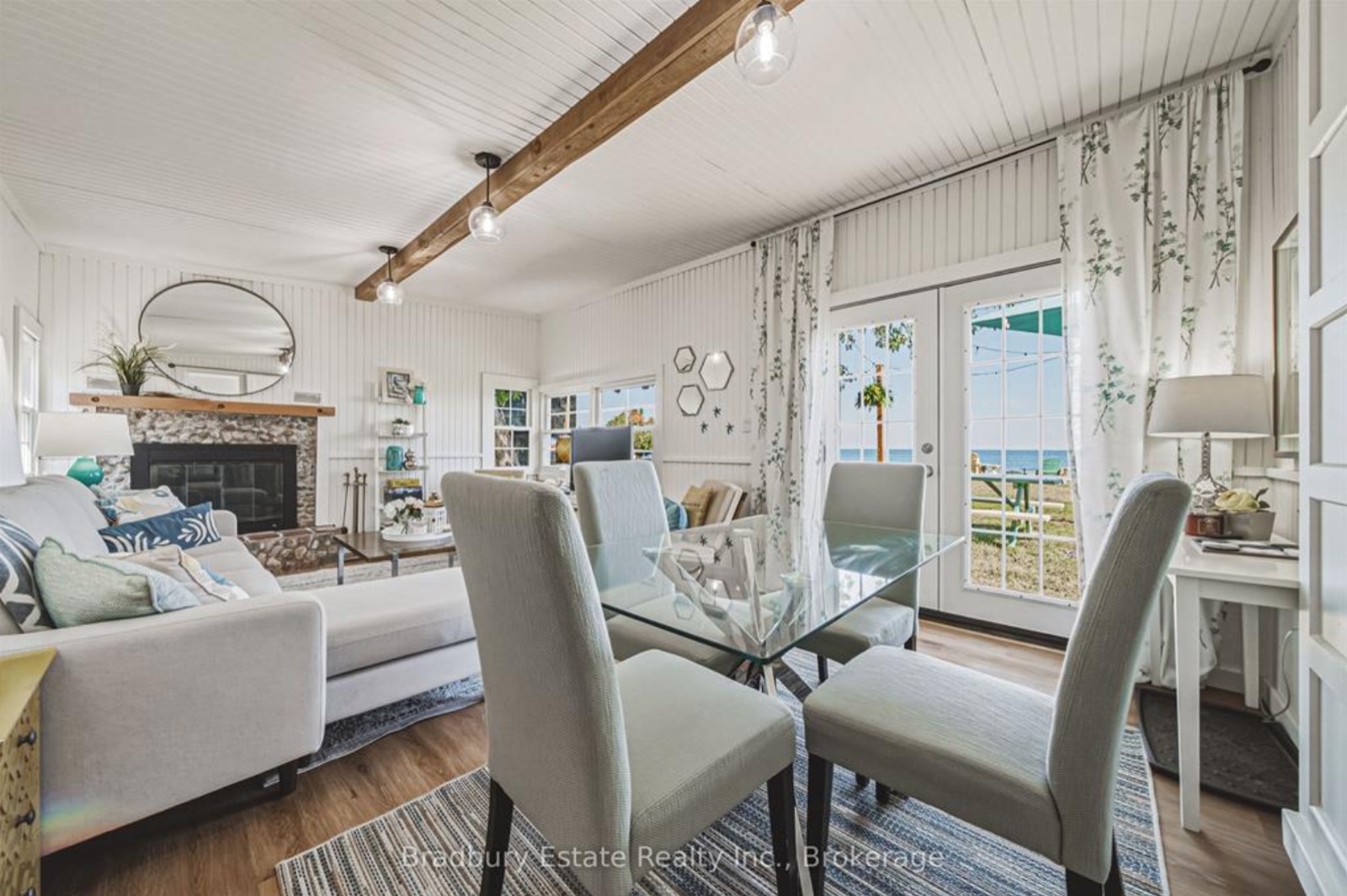 The same living room staged, with a mirror over the fireplace and a dining set by the window
