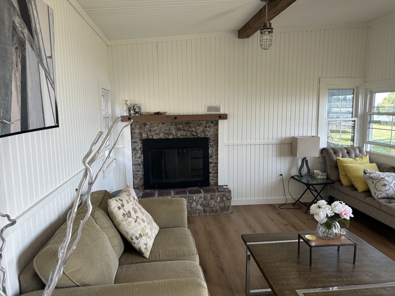 Cottage living room before, sparse furniture around a stone fireplace