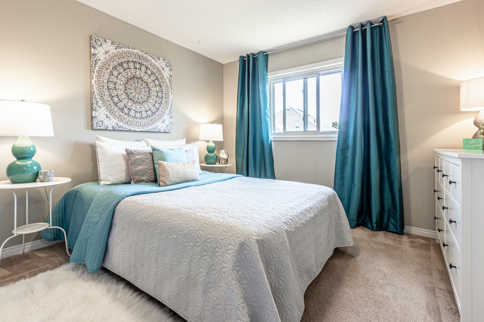 The same bedroom after: warm grey walls, teal curtains, made bed, staged.