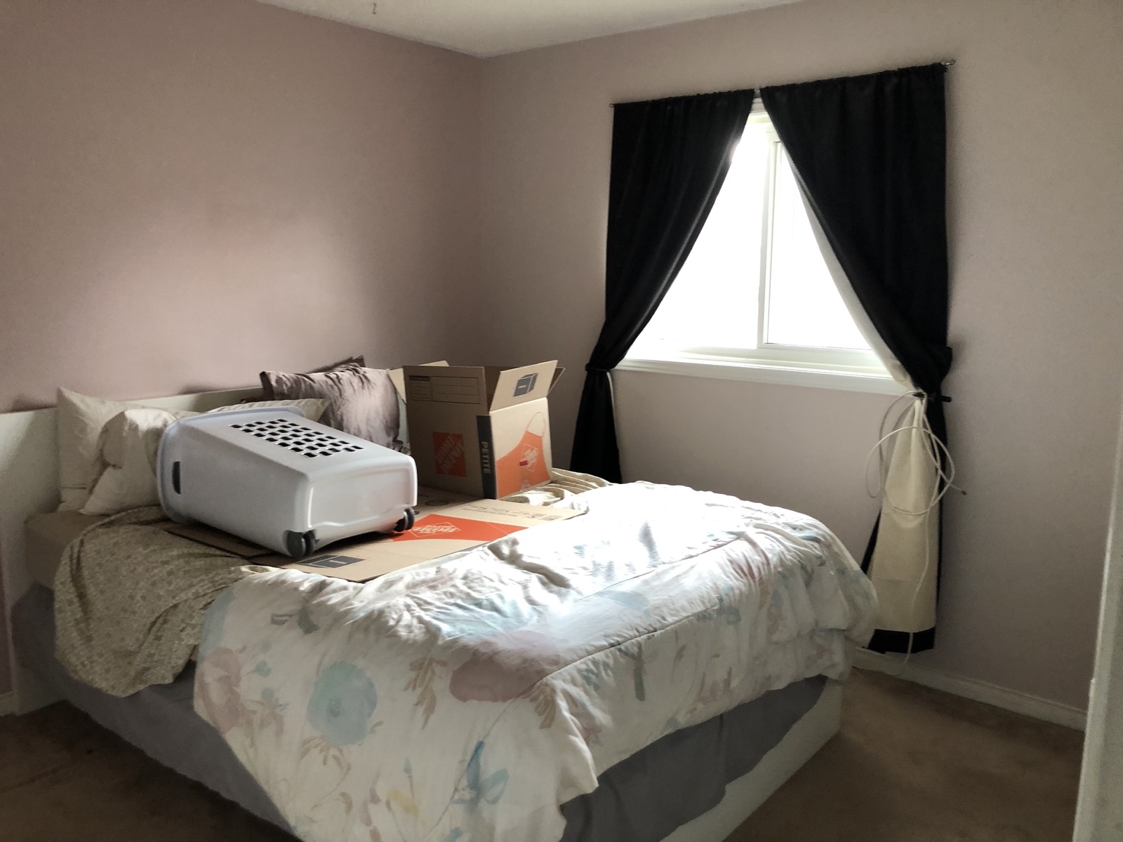 A bedroom before the Giveback: mauve walls, black curtains, boxes on the bed.